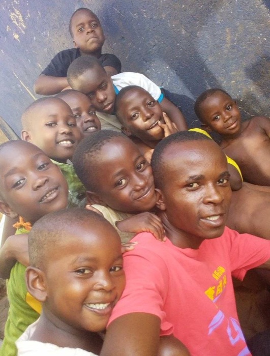 Bugingo, in a pink T-shirt, taking a selfie with ten smiling Desire Kids crowded around and behind him