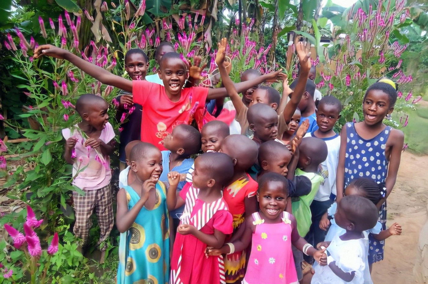 Children of Desire Child Care laughing and waving with their arms raised, standing among tall pink celosia flowers