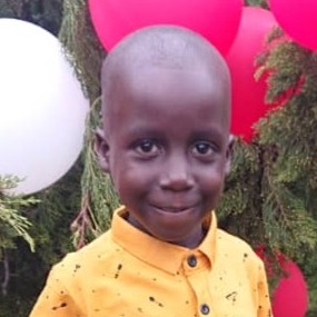 Lubega Kasozi Shafik smiling in a yellow shirt, with red and white balloons behind him