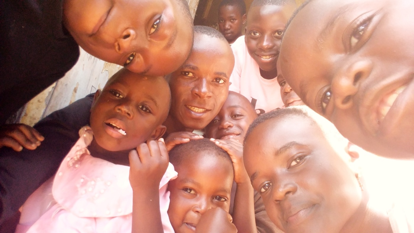 Bugingo "Desire" Moses surrounded by children pressed close to the camera, all of them smiling