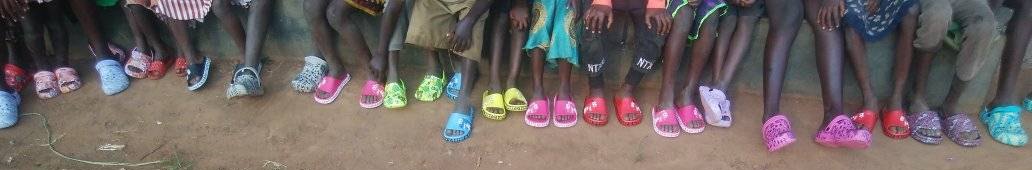 A long row of children's legs and feet, every child in bright new sandals, on red earth